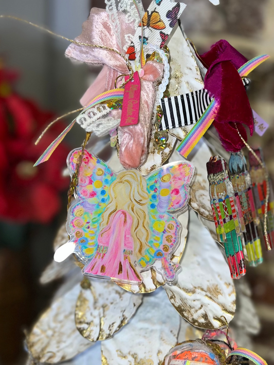 A decorative Christmas tree adorned with colorful ornaments, including a butterfly-shaped ornament, a pink bow, striped ribbon, tassels, and a white star topper, set against a blurred brick wall background.